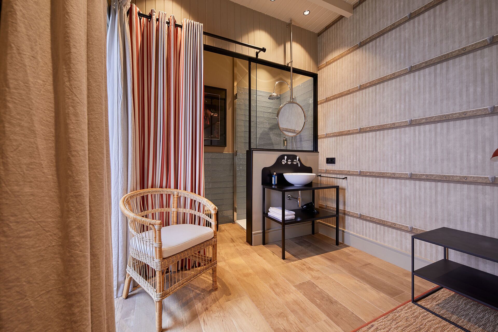 A modern bathroom with a wicker chair, a glass shower enclosure, and a black vanity with a mirror.