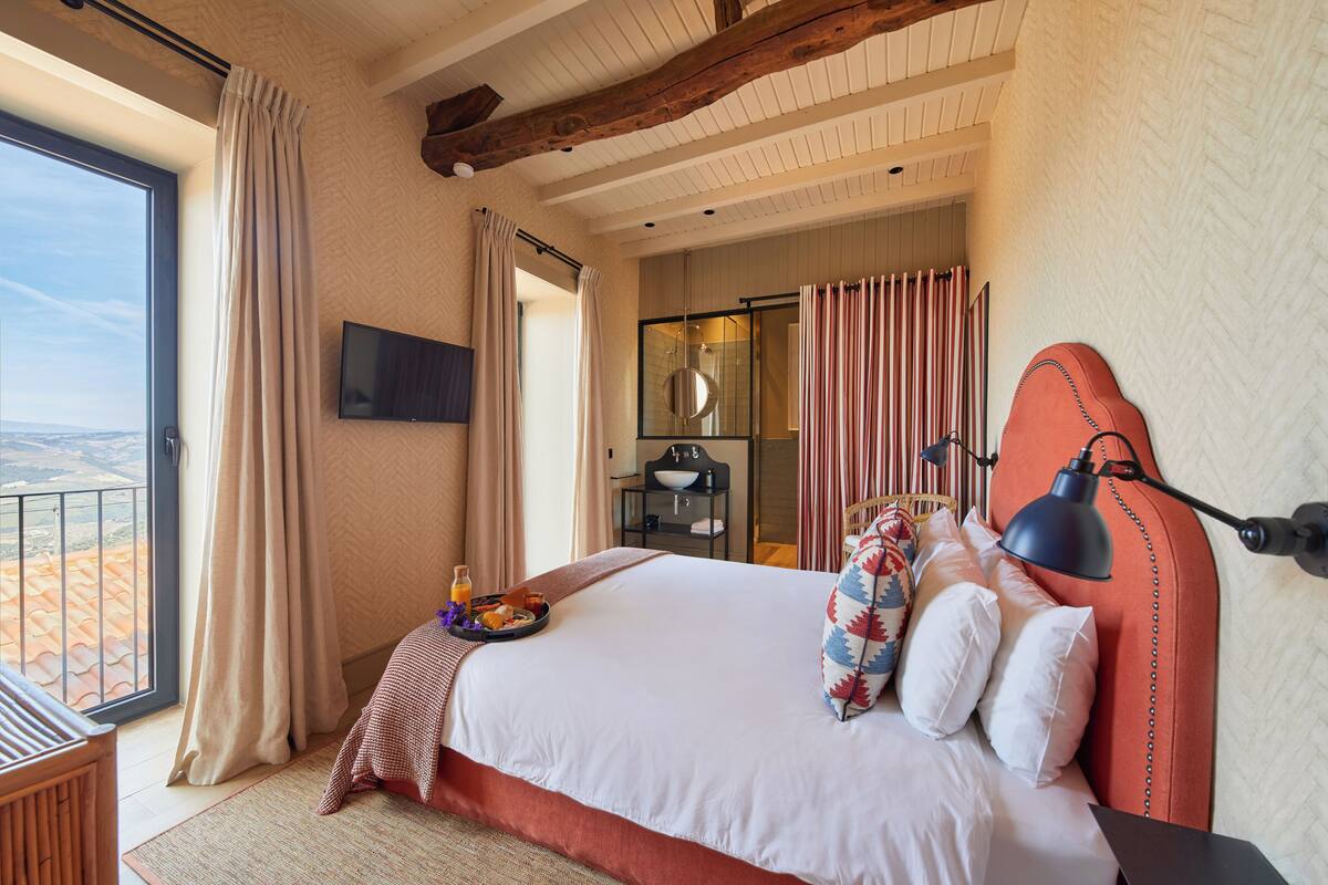 Ein Hotelzimmer mit einem großen Bett, einem Fernseher, einem Badezimmer mit Glastür und Blick auf die Wüste.