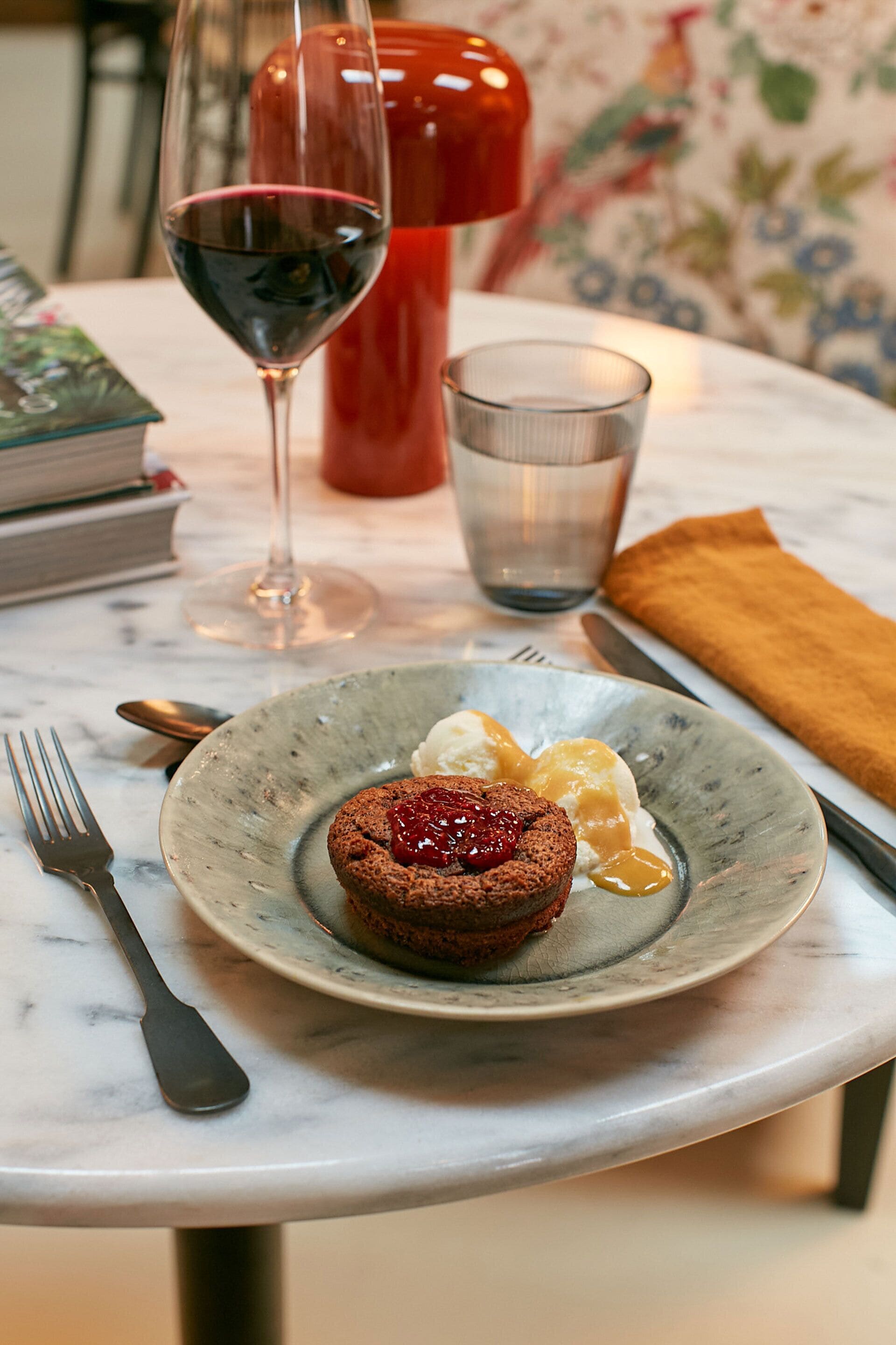 A dessert plate with a chocolate cake, a glass of red wine, and a cup of water on a marble table.