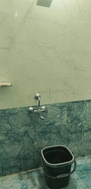 Un baño con pared de mármol, un lavamanos con grifo y un cubo con la etiqueta "NAKODA".