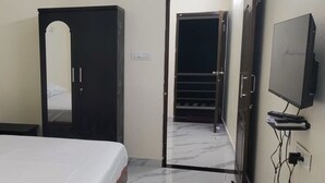 A bedroom with a bed, a wardrobe, a television, and a door leading to a staircase. - Viji Towers Tiruvannamalai (Tiruvannamalai)