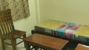 A room with a bed covered in a patterned mattress, a wooden chair, and a small wooden table. - Viji Towers Tiruvannamalai (Tiruvannamalai)