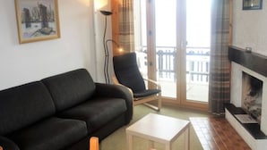 A living room with a black sofa, a wooden chair, a small white table, and a fireplace. - Apartment With Alpine Gateway (Veysonnaz)