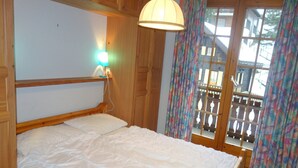A wooden bed with a white mattress in a room with wooden walls and a window with curtains. - Apartment With Alpine Gateway (Veysonnaz)