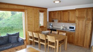 A cozy cabin-style room with a dining table, chairs, a sofa, and a kitchen area with wooden cabinets and a countertop. - Apartment With Alpine Gateway (Veysonnaz)