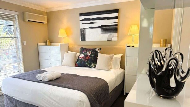 A hotel room with a bed, bedside lamps, a modern abstract painting, and a decorative vase on the nightstand. - 22 Home Sweet Home Coastal Currambine (Currambine)