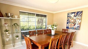 A dining room with a wooden table and chairs, a vase of flowers, and a painting on the wall. - 22 Home Sweet Home Coastal Currambine (Currambine)