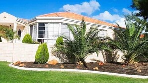 A modern house with a curved roof, large windows, and a well-maintained garden with palm trees and shrubs. - 22 Home Sweet Home Coastal Currambine (Currambine)