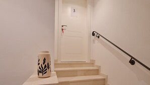 Eine Treppe mit Handlauf, eine Tür mit Nummernschild und ein Blumentopf auf der Zwischenebene.