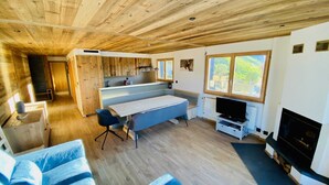Ein modernes Blockhaus-Interieur mit Holzbalkendecke, Essbereich mit Bank, Fernseher und Kamin.