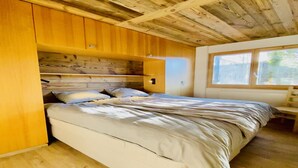 Ein Schlafzimmer mit Holzbalkendecke, einem Bett mit weißer Bettwäsche und einem Fenster, das natürliches Licht hereinlässt.