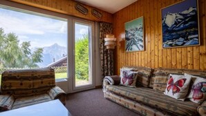 A room with wooden walls, a sofa with butterfly pillows, and a view of mountains through large windows. - Beaulieu F 014 Center Apartment 5 Pers (Veysonnaz)