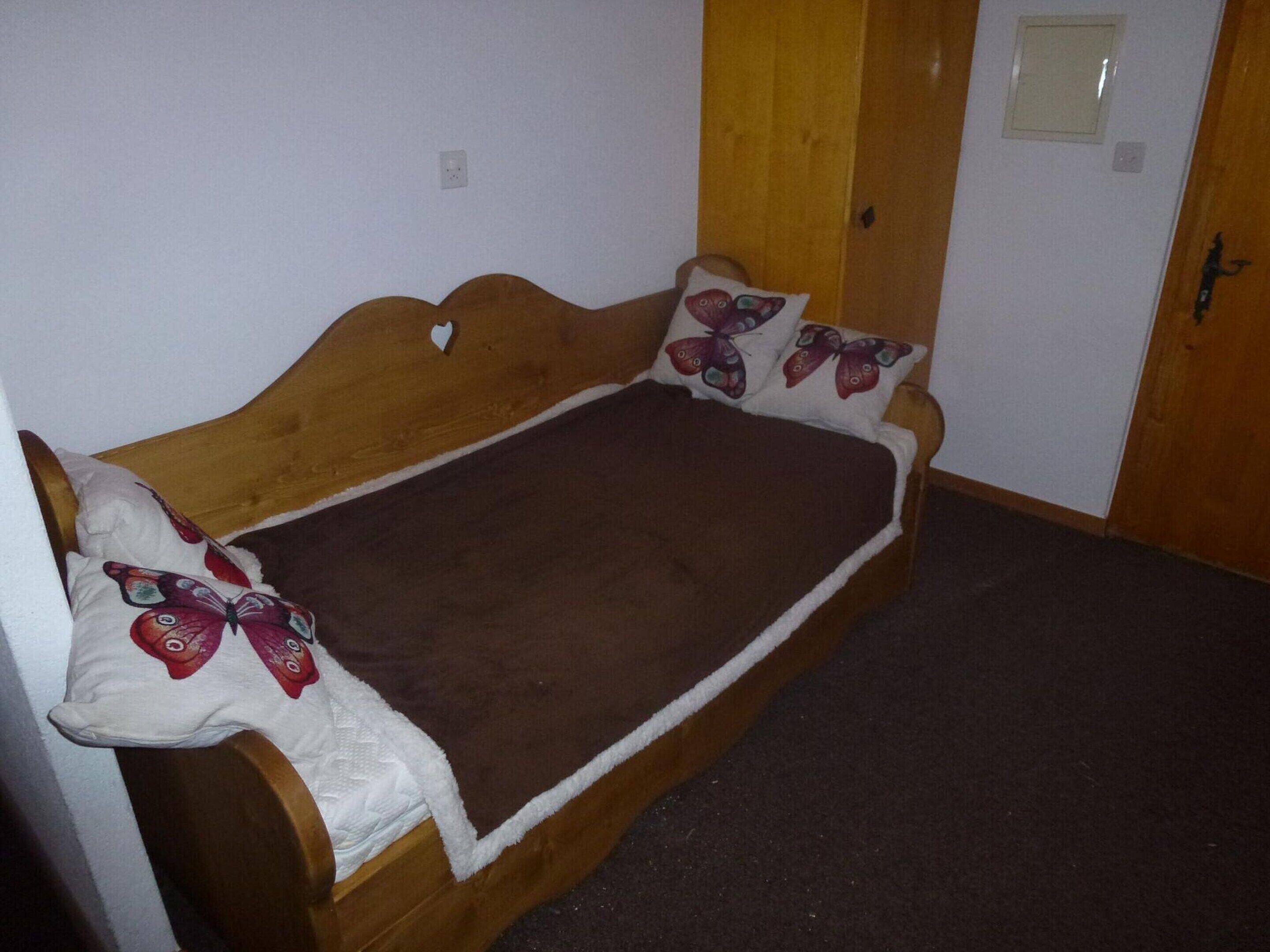 A single bed with a wooden headboard, a brown blanket, and decorative pillows with butterfly designs.