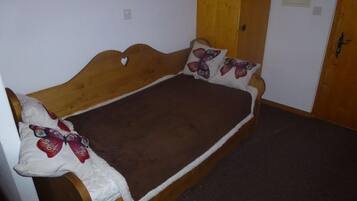 A single bed with a wooden headboard, a brown blanket, and decorative pillows with butterfly designs.