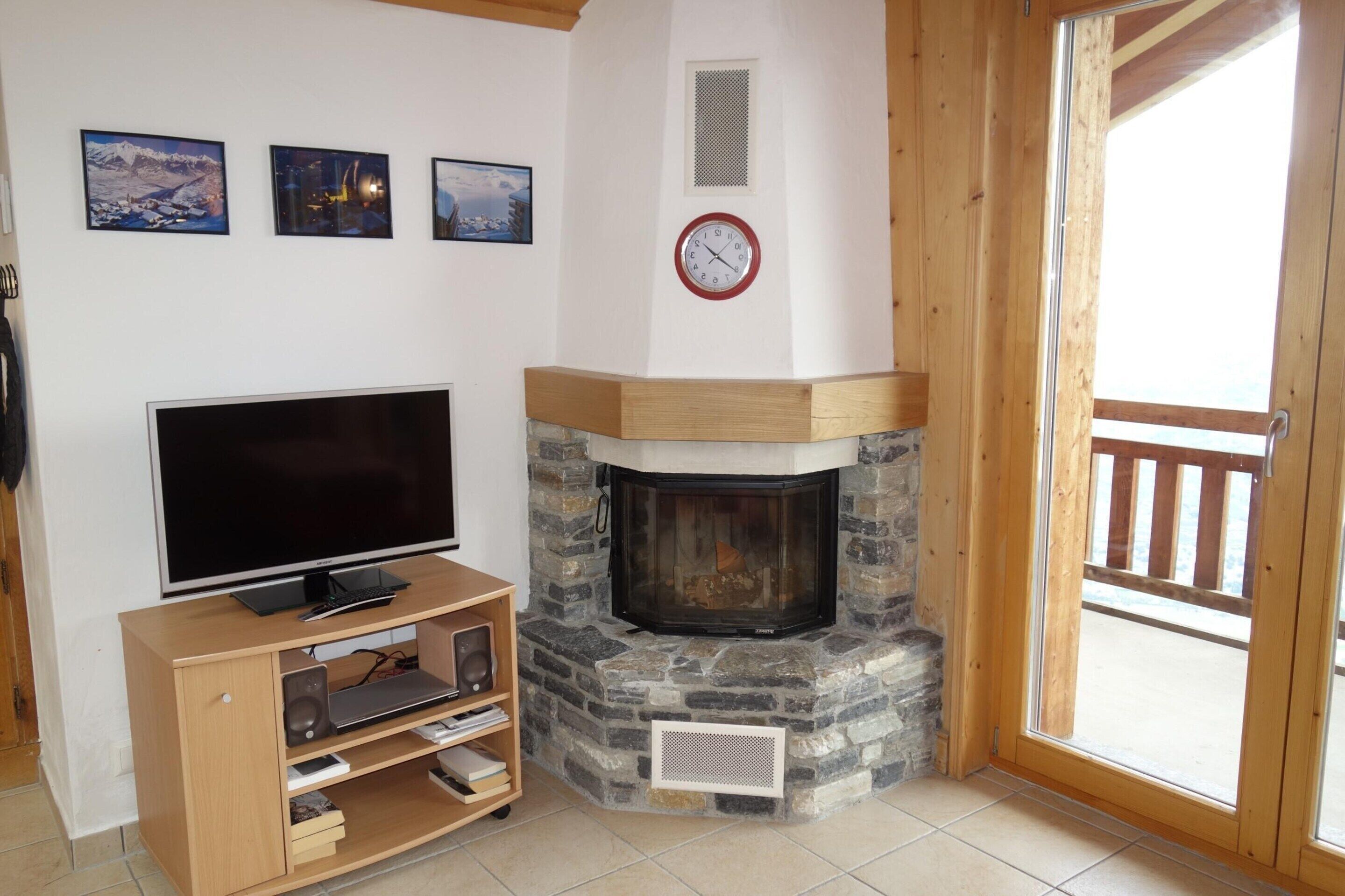 A living room with a fireplace, a television on a wooden stand, and three framed pictures on the wall.