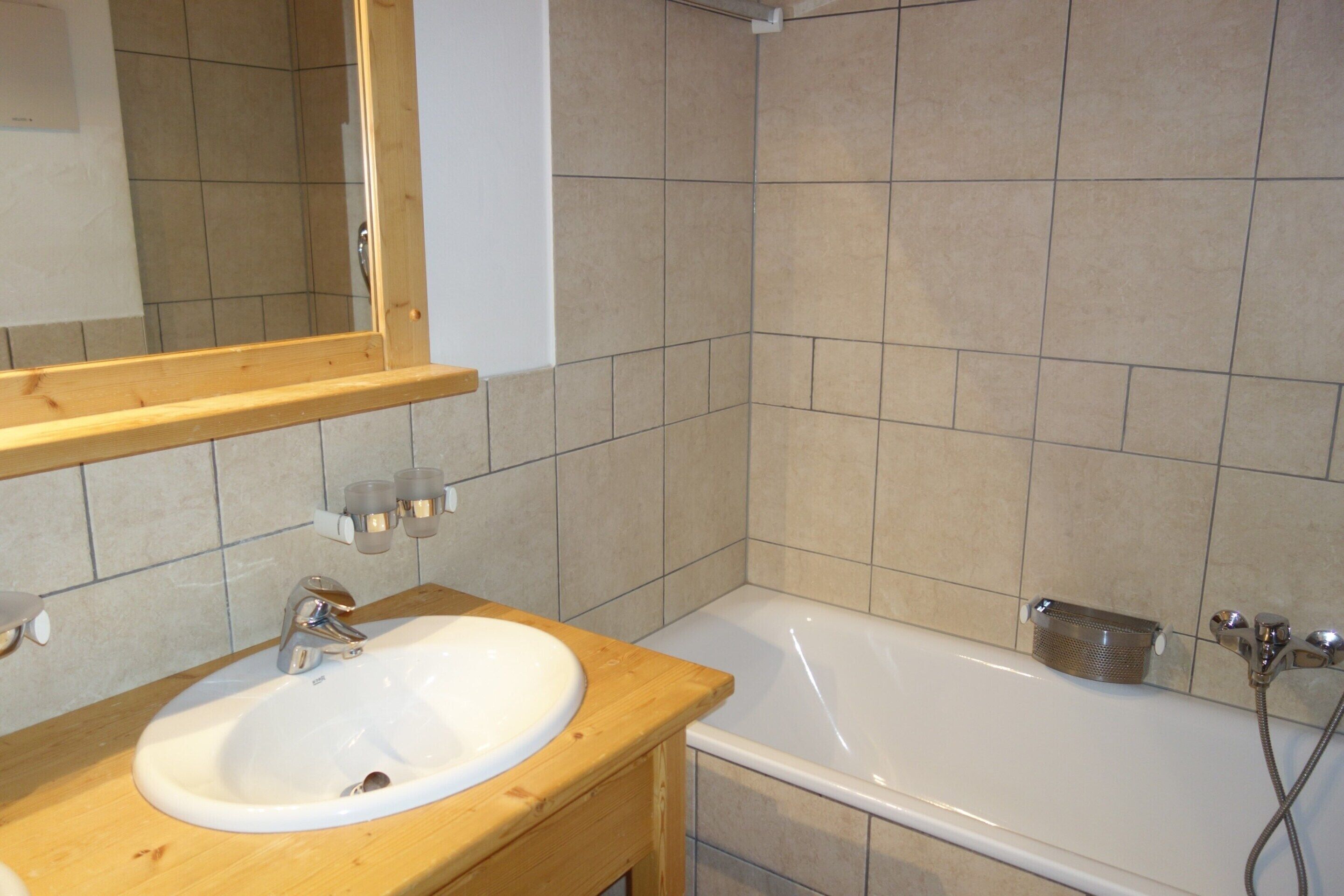 A bathroom with a wooden vanity, a white sink, a mirror, a bathtub, and a shower.