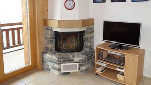 A cozy living room with a stone fireplace, a television, and a wooden entertainment unit. - Hilltop Apartment With Views (Veysonnaz)