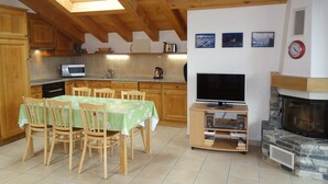A kitchen with wooden cabinets, a dining table with chairs, a microwave, a kettle, and a television on a wooden stand. - Hilltop Apartment With Views (Veysonnaz)