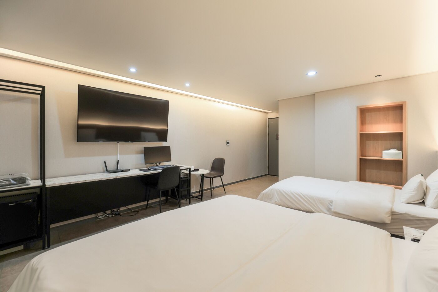 Habitación de hotel con dos camas, un escritorio con computadora, una silla, televisor y estante de madera.