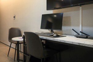 Un espacio de trabajo moderno con un monitor de pantalla plana grande, un teclado, un ratón y un router inalámbrico sobre una encimera de mármol. Hay dos sillas negras y una mesa redonda pequeña.