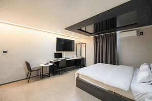Une chambre d’hôtel moderne équipée d’un lit, d’un bureau avec un ordinateur, d’une chaise et d’un grand miroir.