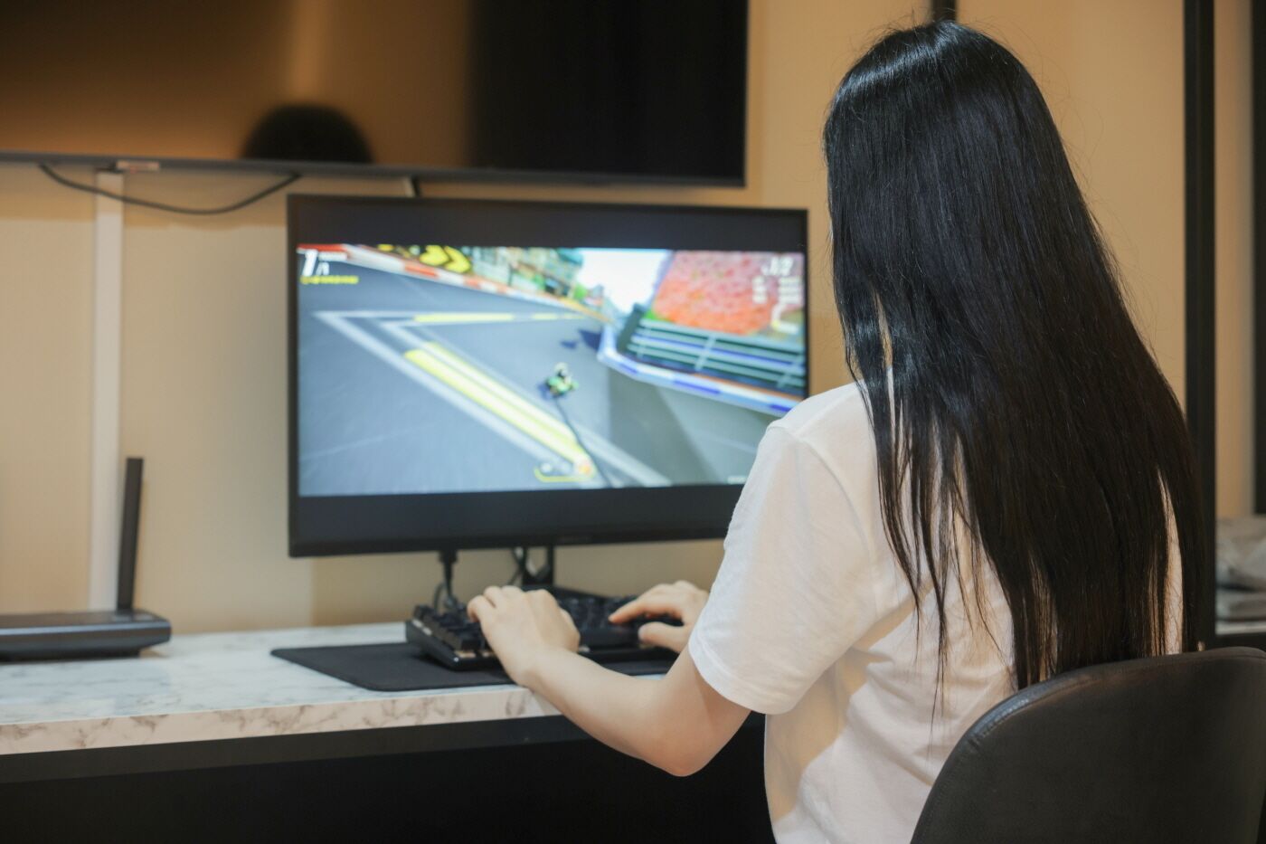 Iemand zit aan een bureau, een computerscherm toont een racespel.
