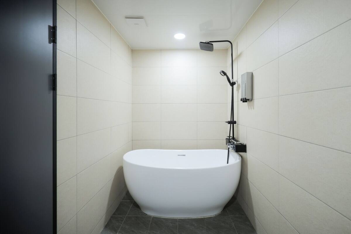 Een moderne badkamer met een vrijstaand bad, een handdouche en een bedieningspaneel aan de muur.
