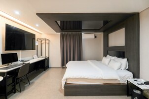 Una habitación de hotel moderna con cama, escritorio y un televisor de pantalla plana grande.