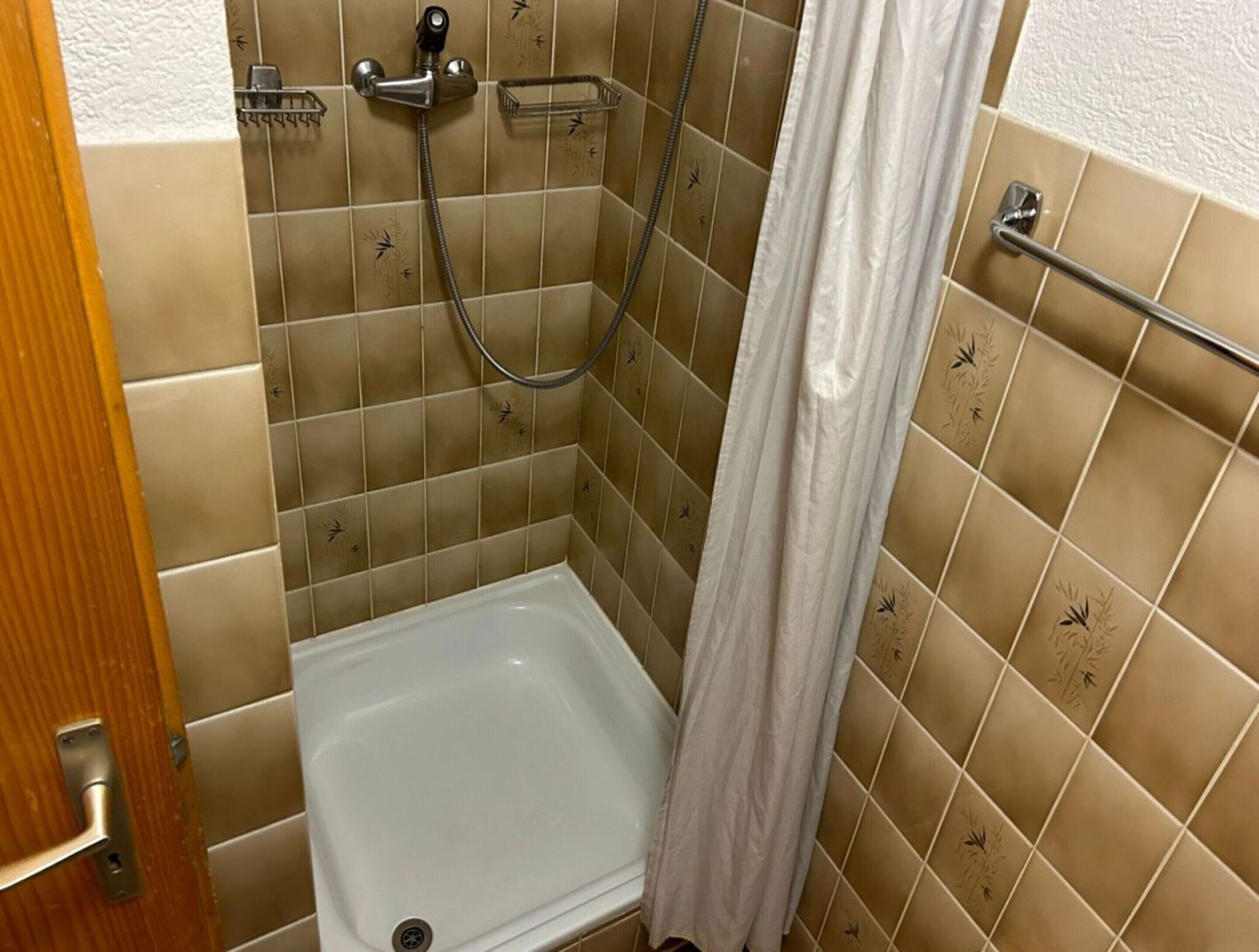 A shower area with a white bathtub, a showerhead, and a handrail.