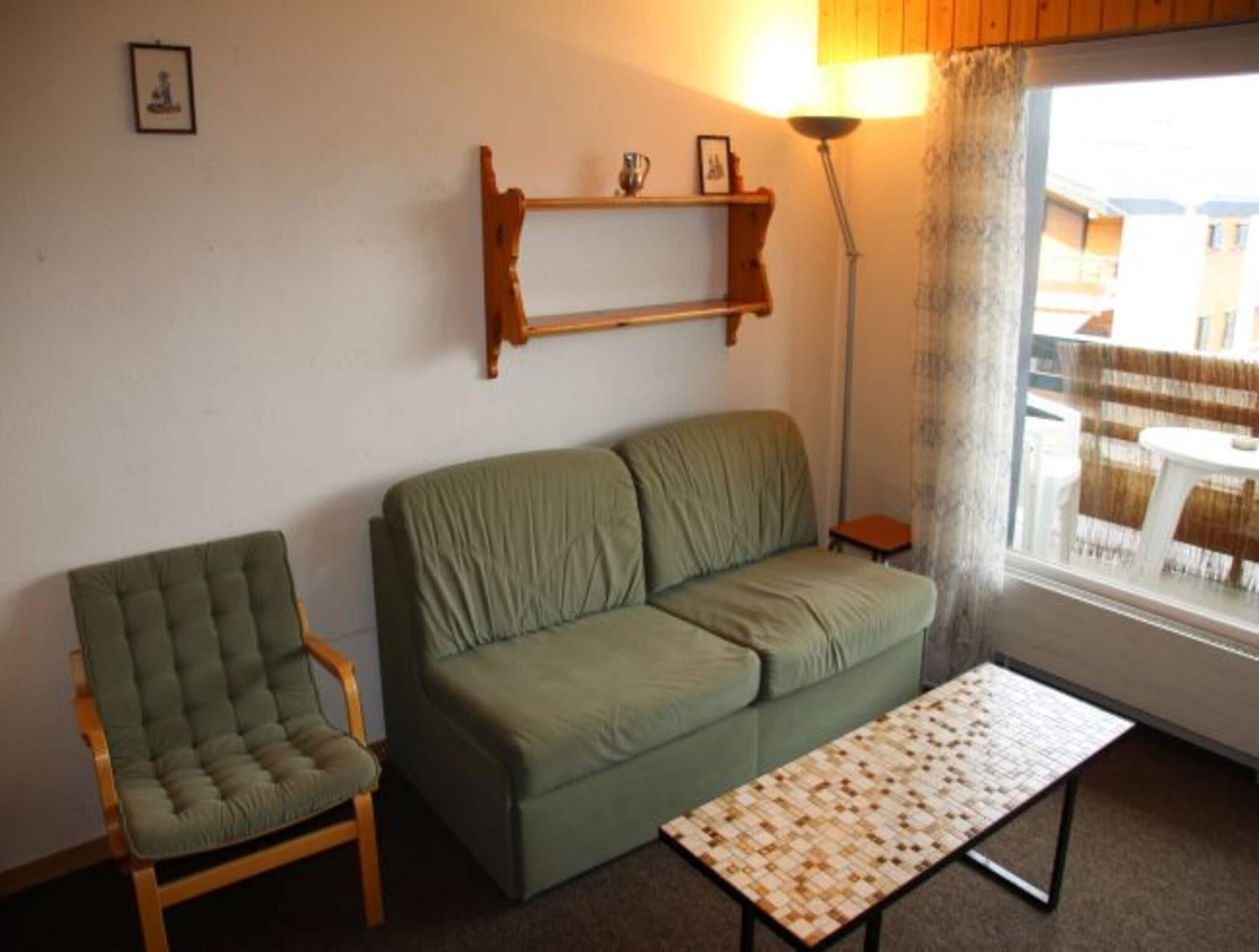 A living room with a green sofa, a matching armchair, a small table, and a lamp.