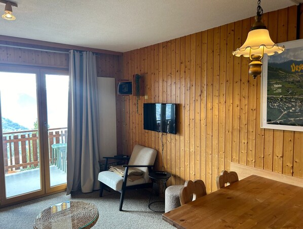 Une pièce aux murs recouverts de lambris en bois, avec un téléviseur fixé au mur, une table à manger et une chaise.