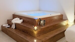 A modern bathroom with a wooden staircase leading to a hot tub. There are towels, slippers, and a bucket on the steps. - Dimora Bianca Luxury (Conversano)
