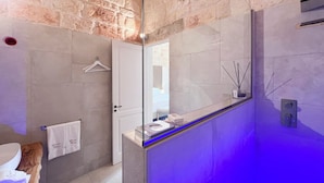 A modern bathroom with a stone wall, a glass shower enclosure, and a towel rack with a hanging towel. - Dimora Bianca Luxury (Conversano)