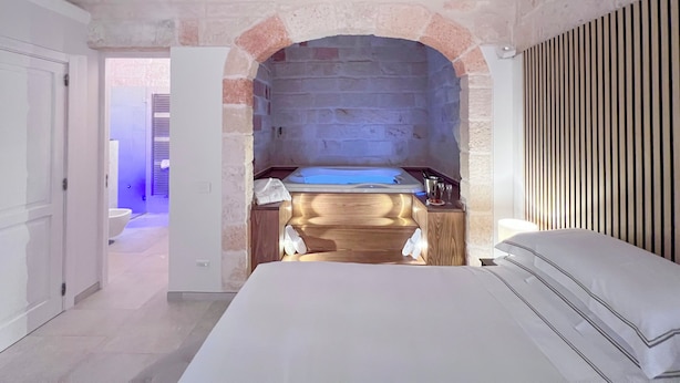 A bedroom with a stone archway, a wooden vanity, and a bed with white linens. - Dimora Bianca Luxury (Conversano)
