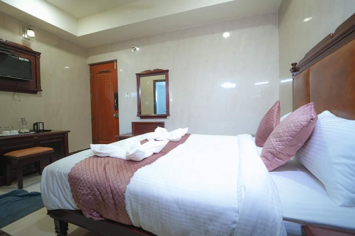 Habitación de hotel con una cama, cabecera de madera, mesita de noche, espejo y armario de madera.