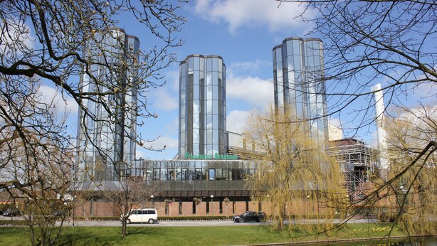 A modern building with a glass facade, surrounded by a park with a pond and trees.