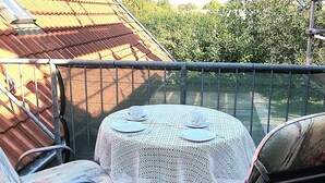 A round table with a white lace tablecloth, two chairs with floral upholstery, and a metal railing.