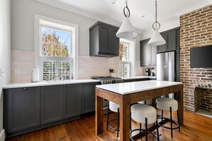 Une cuisine moderne avec des meubles de couleur sombre, un îlot central doté de tabourets, un mur d’accent en briques et une grande fenêtre.