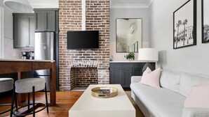 A modern living room with a brick fireplace, a white sofa, and a flat-screen TV mounted on the wall. - Thomas Waring House | Unit B | Sleeps 4 (Charleston)