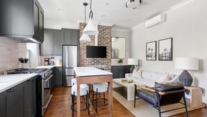 A modern kitchen with a large island, bar stools, and a dining area with a sofa and coffee table. - Thomas Waring House | Unit B | Sleeps 4 (Charleston)