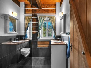 A modern bathroom with two sinks, a toilet, and a shower. It features wooden ceiling beams, large windows with curtains, and a view of greenery outside. - Horni Marsov Khk320 Comfortable Holiday Residence (Horni Marsov)