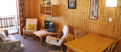 Une pièce chaleureuse avec des murs en bois, un canapé, une table à manger avec des chaises, un téléviseur et une bibliothèque.