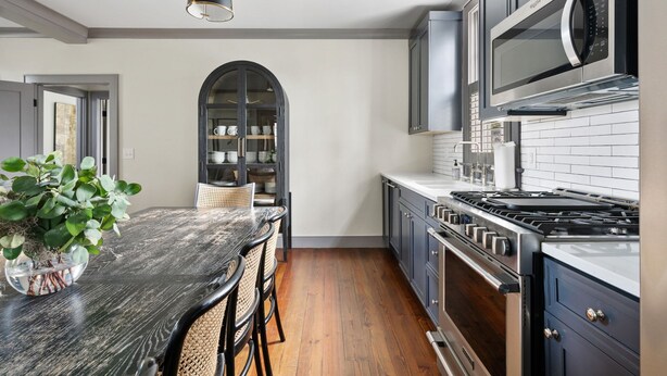 A modern kitchen with dark cabinets, a stainless steel stove, and a large island with chairs. - Rosemary House - C | Perfect for Weddings + Events (Charleston)