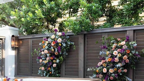 Un área de estar con mobiliario de mimbre y una mesa de vidrio, junto a un arreglo floral.