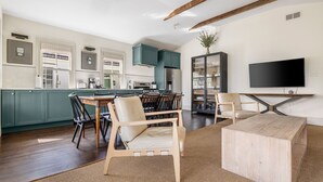 Una cocina moderna con armarios color esmeralda, un comedor con sillas de madera, una gran mesa de centro de madera y un televisor de pantalla plana montado en la pared.
