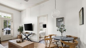 A modern living room with a wooden coffee table, a TV mounted on the wall, a dining table with wooden chairs, and a large window with a view of greenery. - Harleston House, Unit B, Sleeps 6 (Charleston)