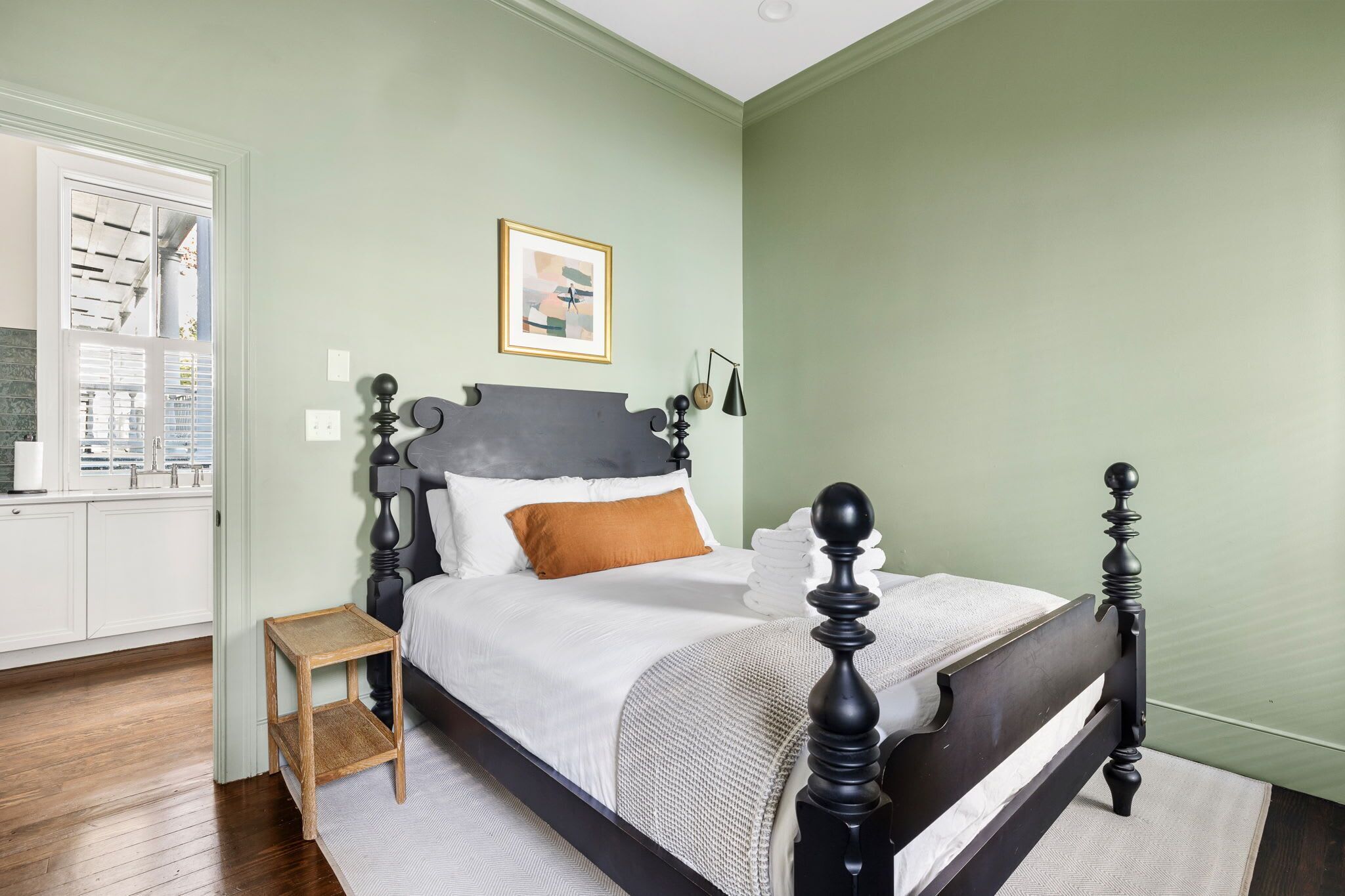 A bedroom with a bed, a nightstand, a framed picture on the wall, and a window with blinds.