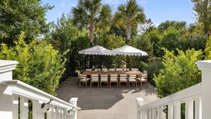 A patio with a wooden table and chairs, surrounded by lush greenery and palm trees. - Harleston House, Unit B, Sleeps 6 (Charleston)