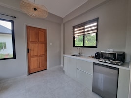 Una cocina compacta con puerta de madera, ventana con persianas, un lavamanos, microondas y lavavajillas.