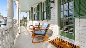 A porch with white columns, green shutters, and two rocking chairs. - The Gardenia House | Sleeps 20 | Multi-Unit Rental (Charleston)